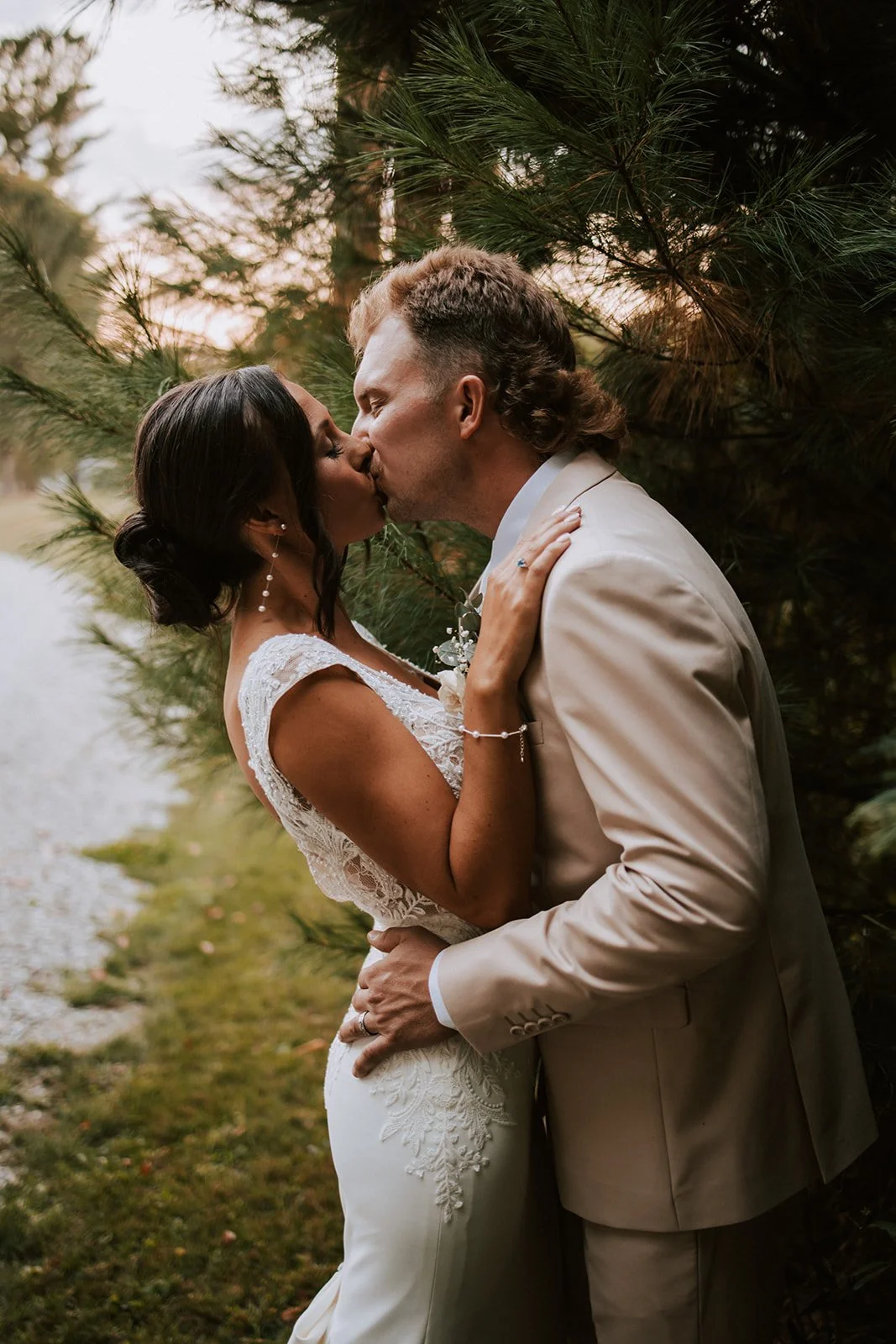 A bride and groom sharing a kiss outdoors, surrounded by trees and natural scenery.