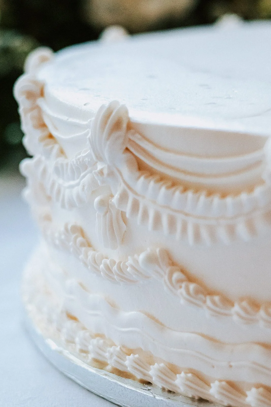 Close-up of a white wedding cake with intricate piping and decorative icing details.