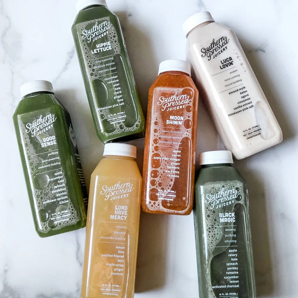 Six bottles of Southern Pressed Juicery juices with different flavors, including Hippe Lettuce, Luca Lovin', Moon Shinin', Good Sense, Lord Have Mercy, and Black Magic, placed on a white marble surface.