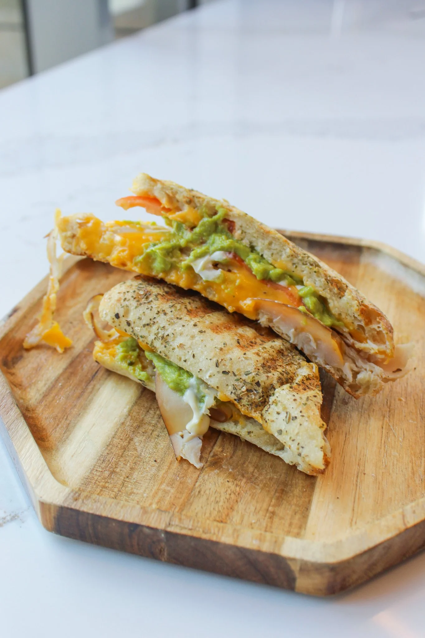Half-cut sandwich with cheese, avocado, tomatoes, and chicken on a wooden tray.