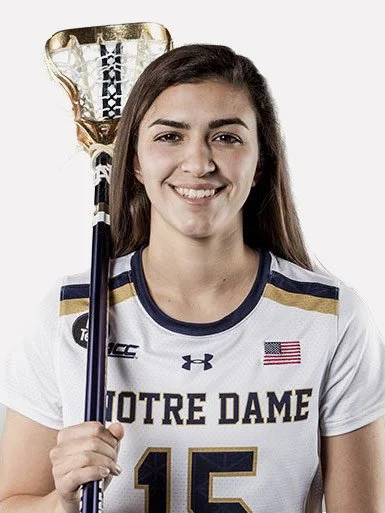 A female lacrosse player in a Notre Dame jersey holding a lacrosse stick.