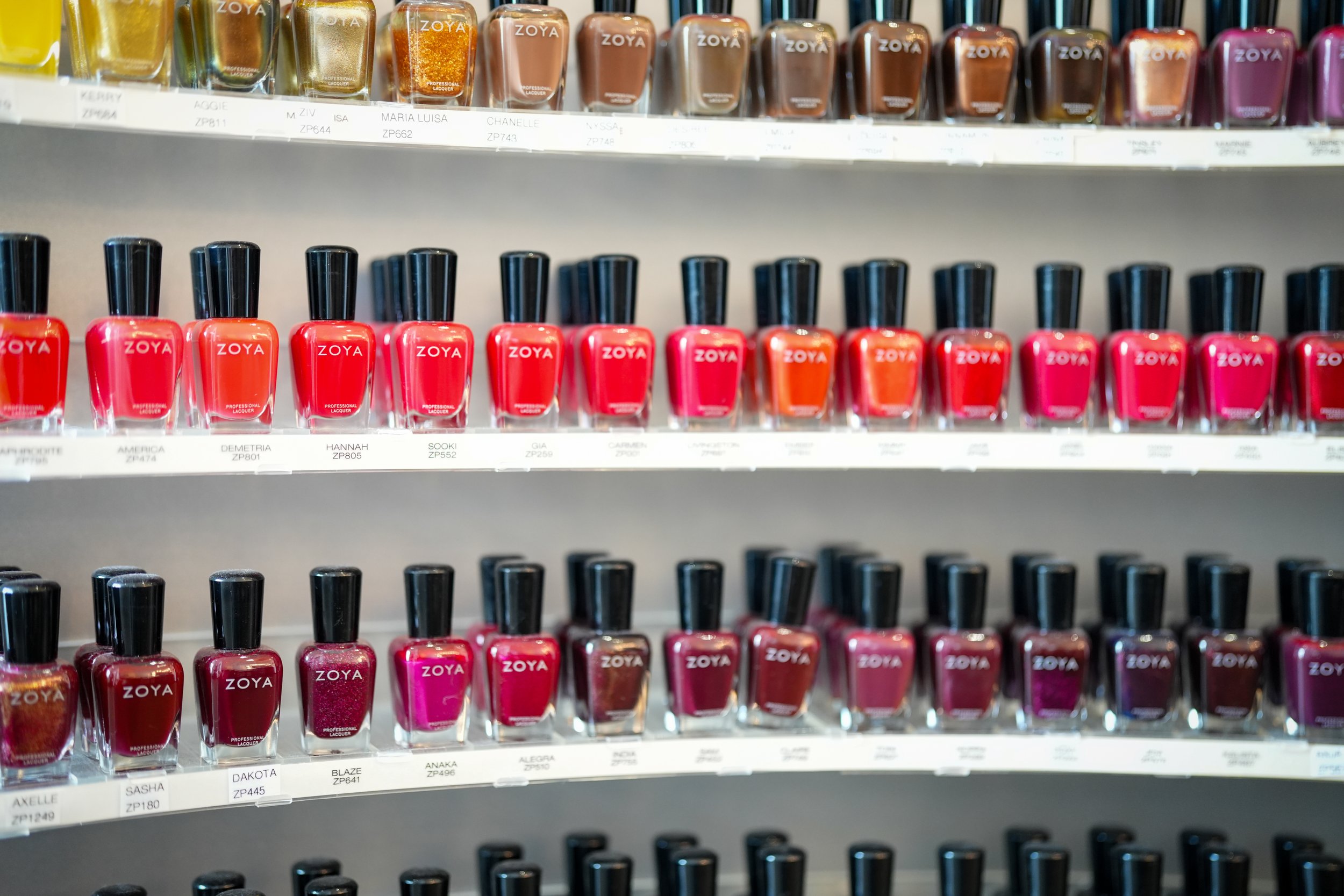 A display shelf of various shades of Zoya brand nail polish bottles arranged in rows at a retail store.