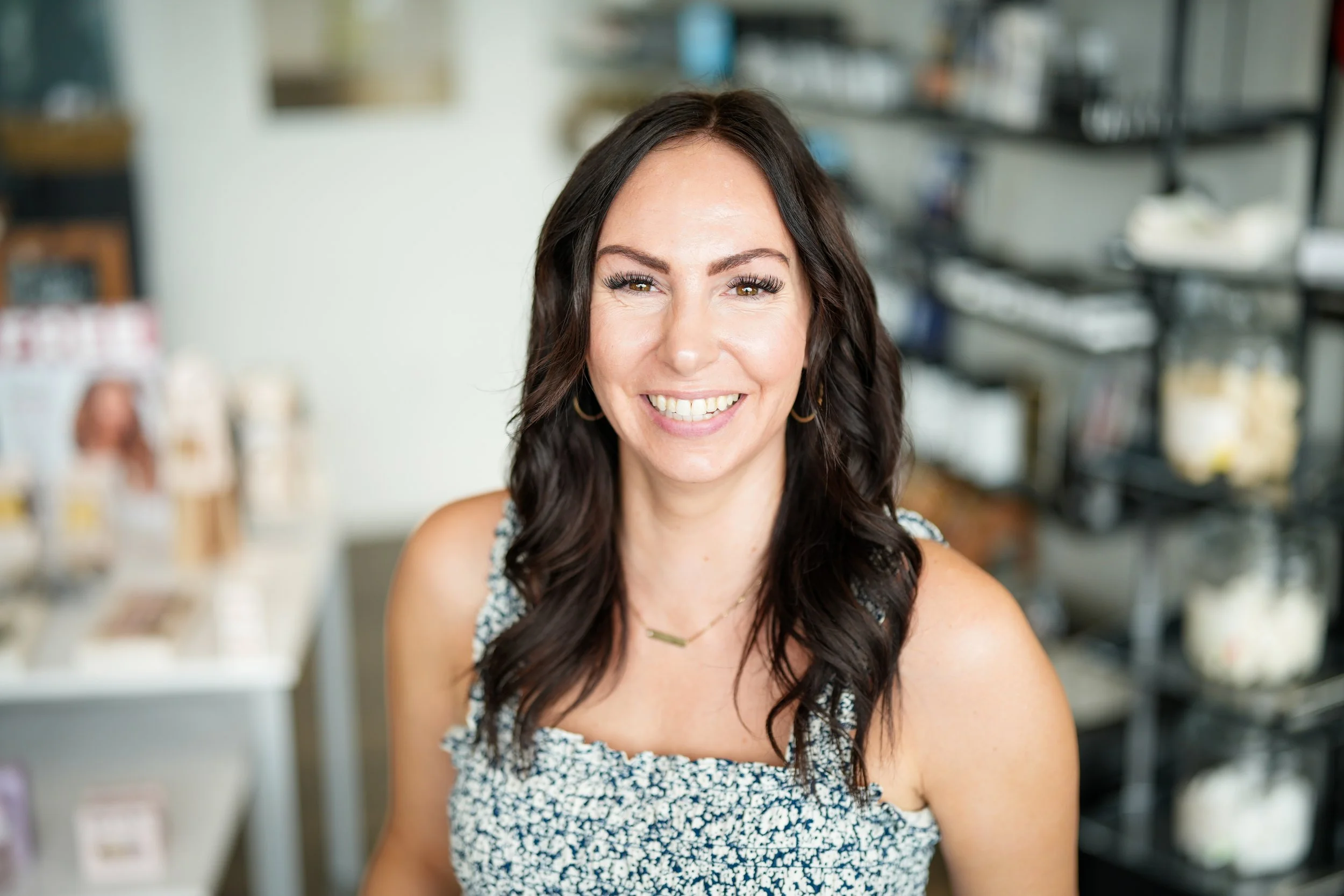 Smiling woman with dark wavy hair wearing a sleeveless patterned top in a store.