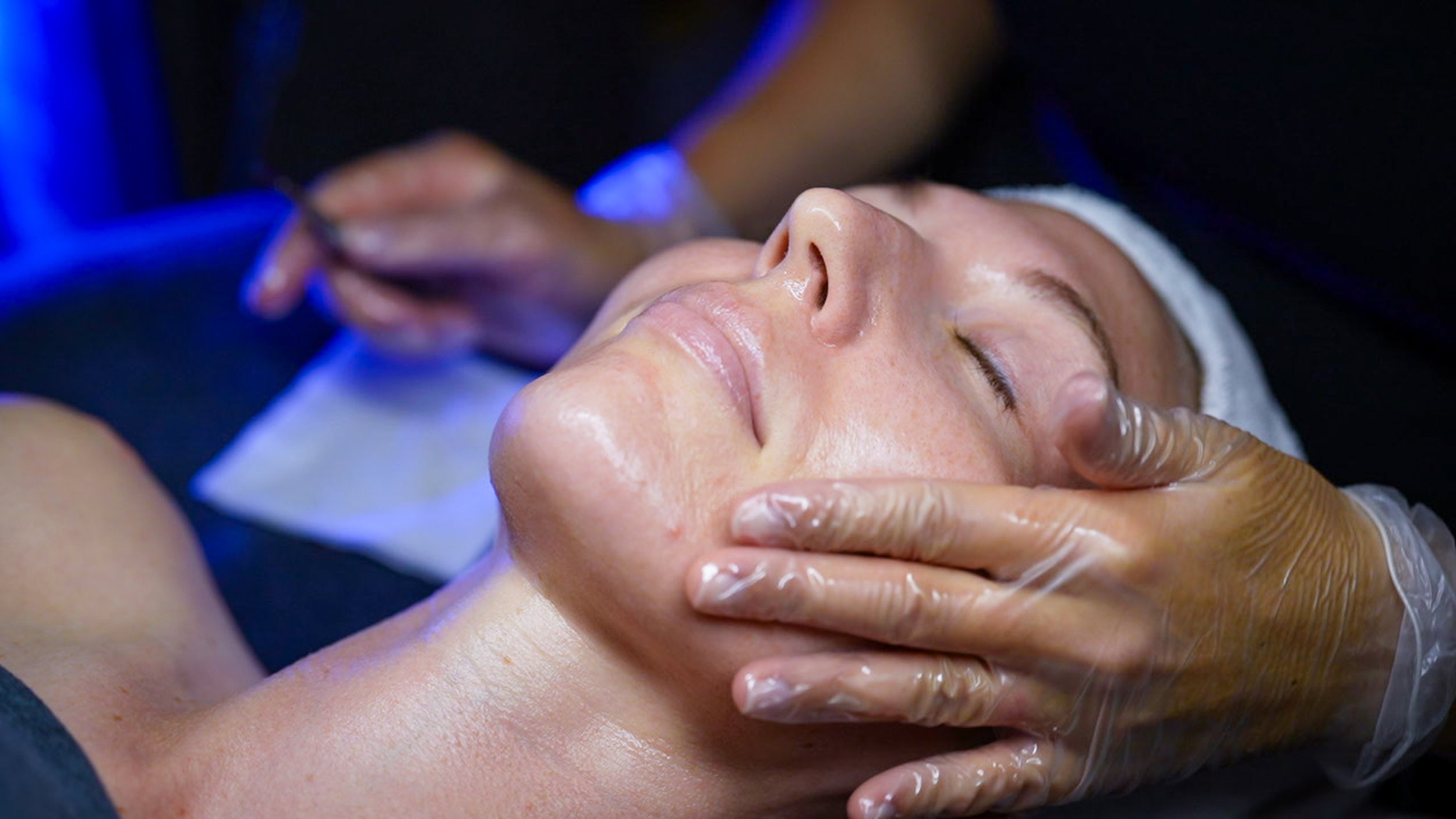 A person receiving a facial massage or treatment in a spa or skincare setting, with a person wearing gloves applying or massaging skincare products on their face.