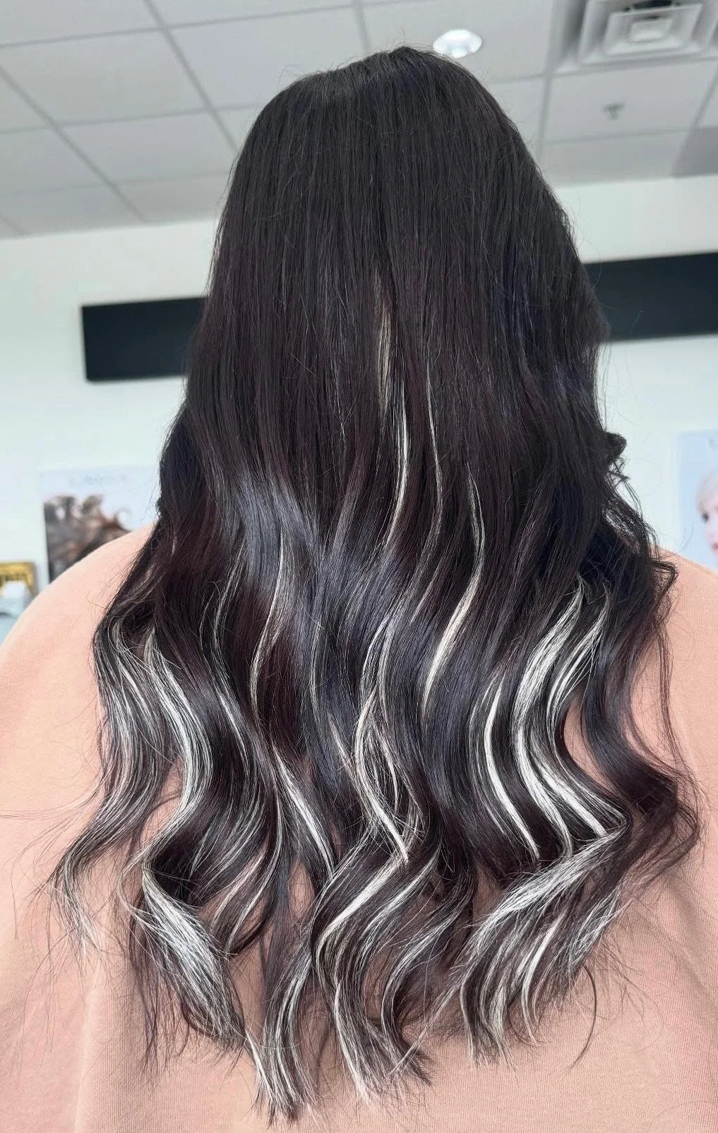 Back view of a person with long black hair accented with white highlights styled in loose waves.