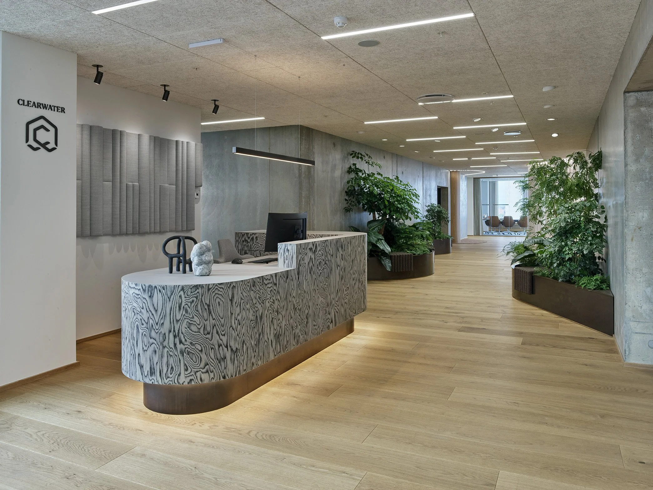 Indendørs moderne kontorlokale med reception, grønne planterne, træloft og store vinduer i baggrunden.