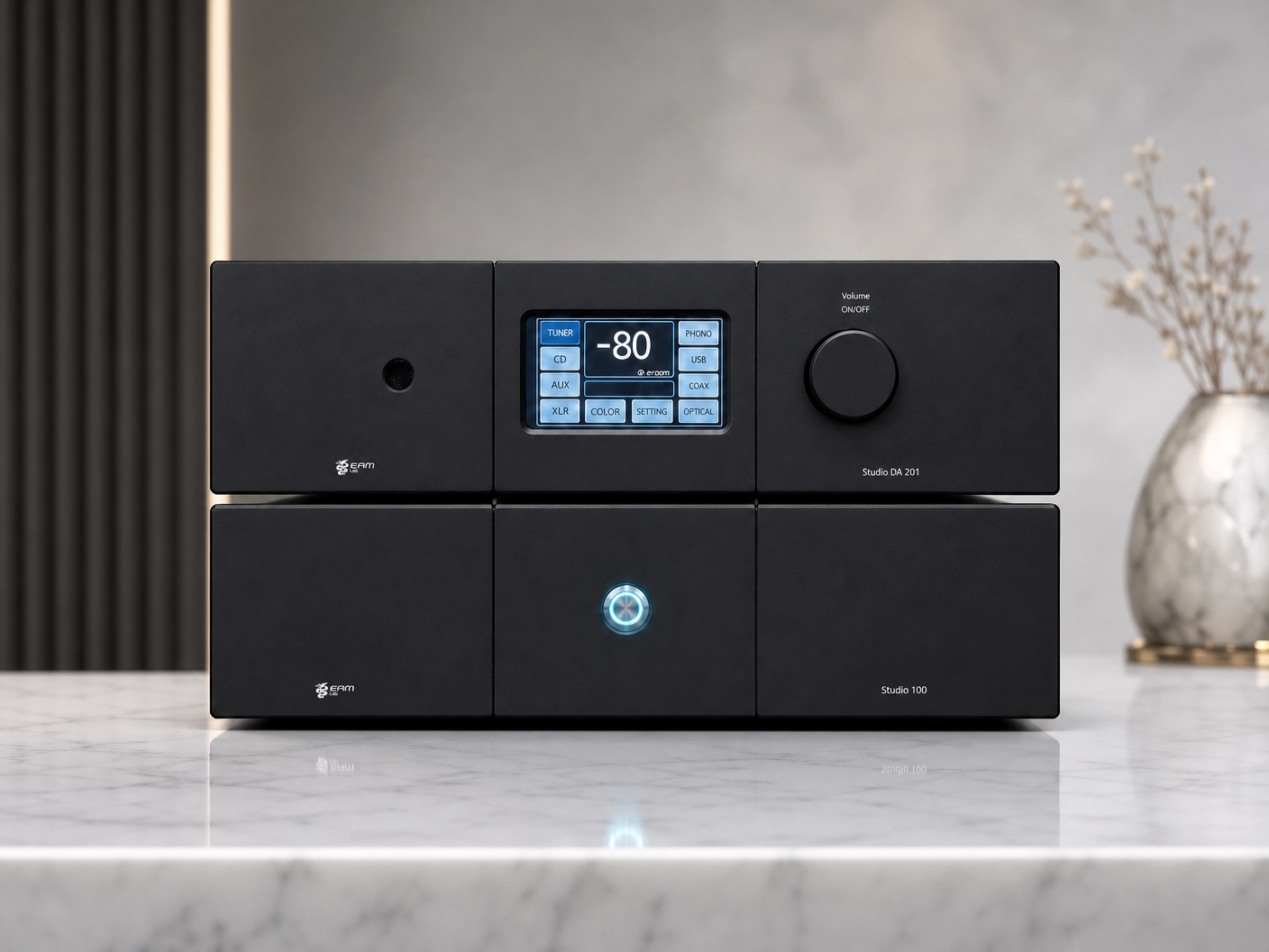 Sistema audio nero con display digitale, volume rotativo, e vari tasti e prese, posizionato su un tavolo di marmo