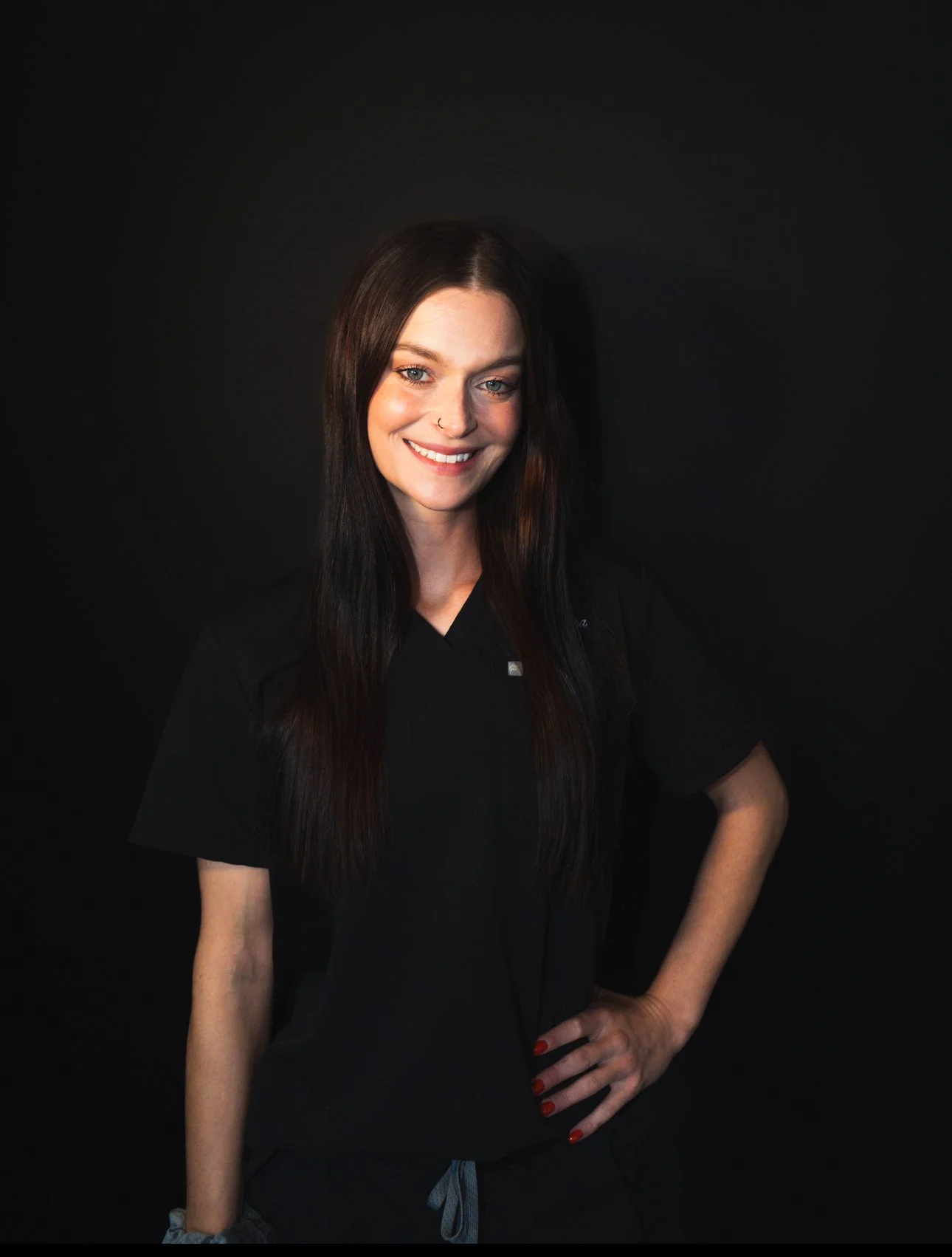 Interior of a pastel pink cafe with a tufted pink bench, a round table with a small plant, and two chairs. The counter area displays a menu board and various cake covers and decorative items.
