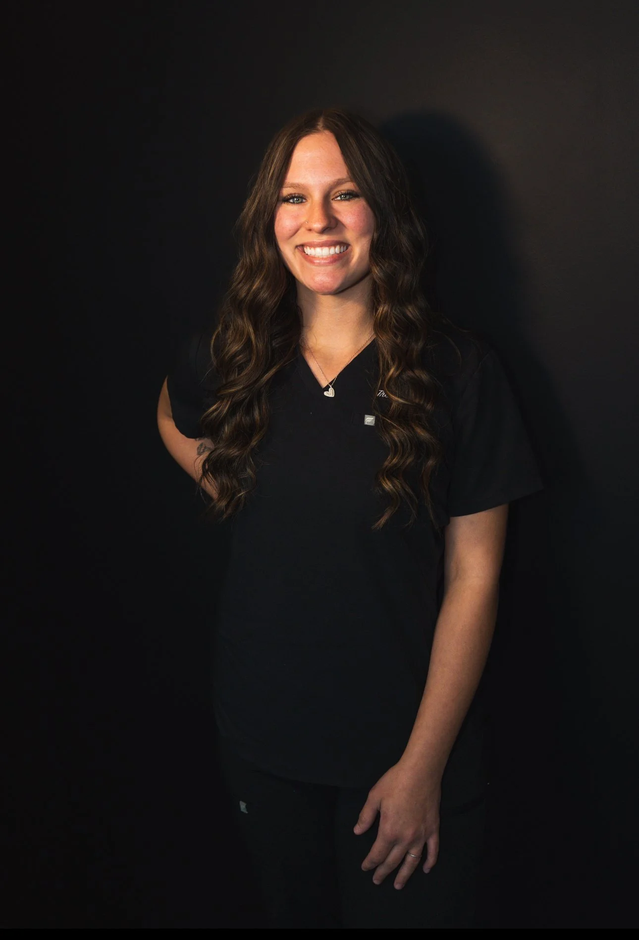 Interior of a pink-themed café with a pink tufted bench, a round table with a flower vase, two beige chairs, and a counter with glass cake displays and a menu board.