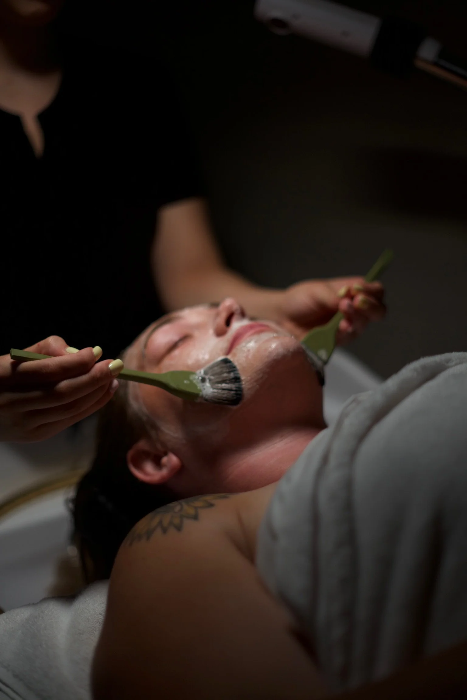 Person with long dark hair lying face down in a spa or massage bath, with water pouring over their head from a circular overhead shower.