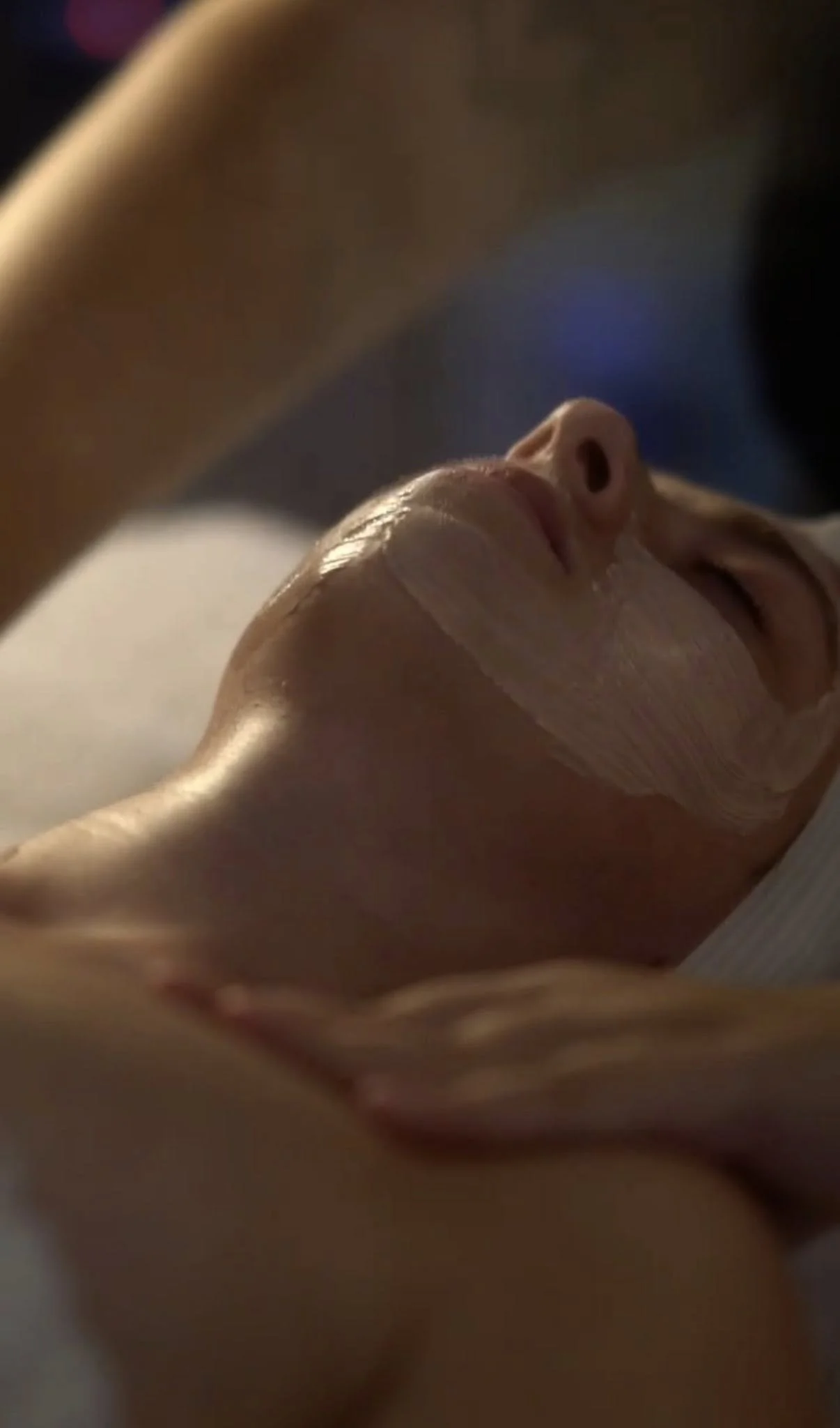 A woman lying down with her eyes closed, her head turned to the side, and a bandage around her chin.