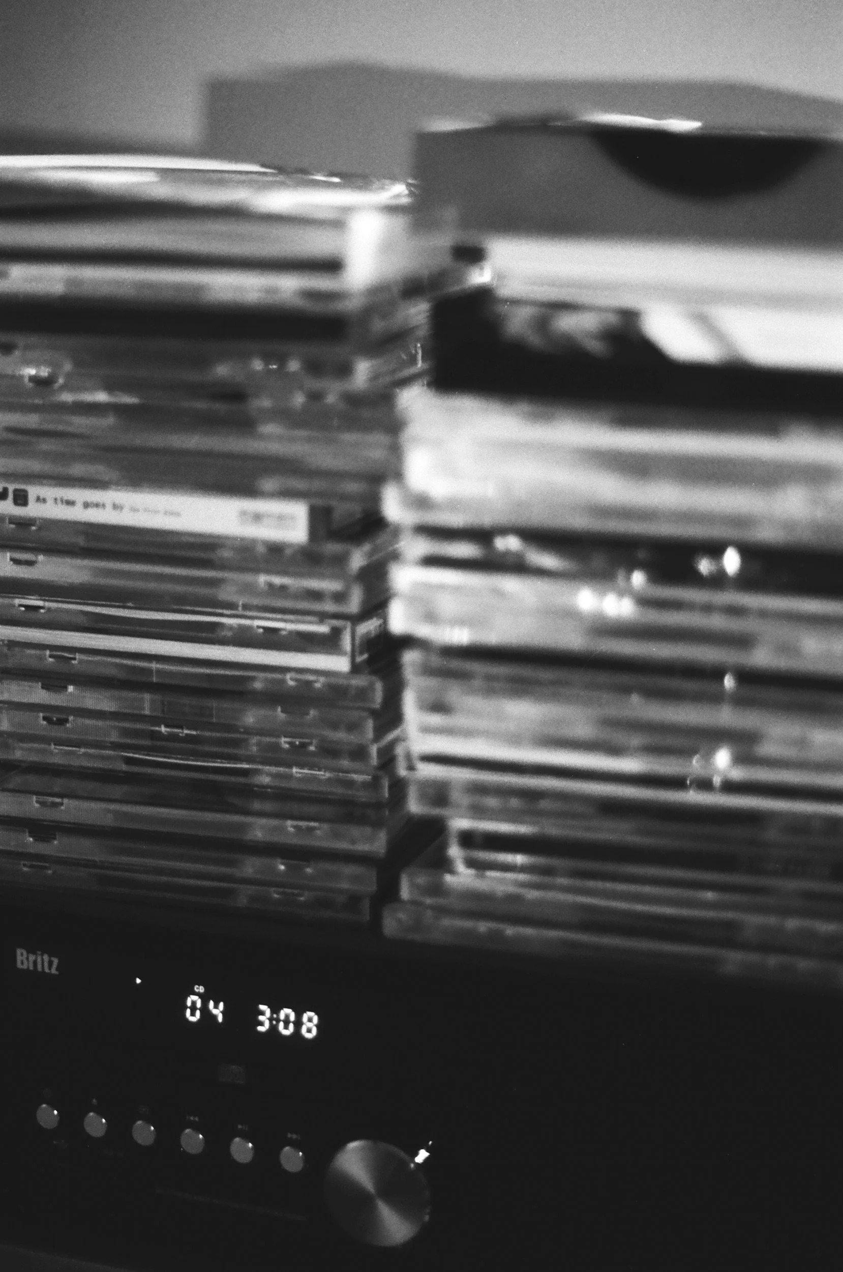 A black and white photo of a stack of CDs on top of a stereo system with a digital display showing 04 3:08.