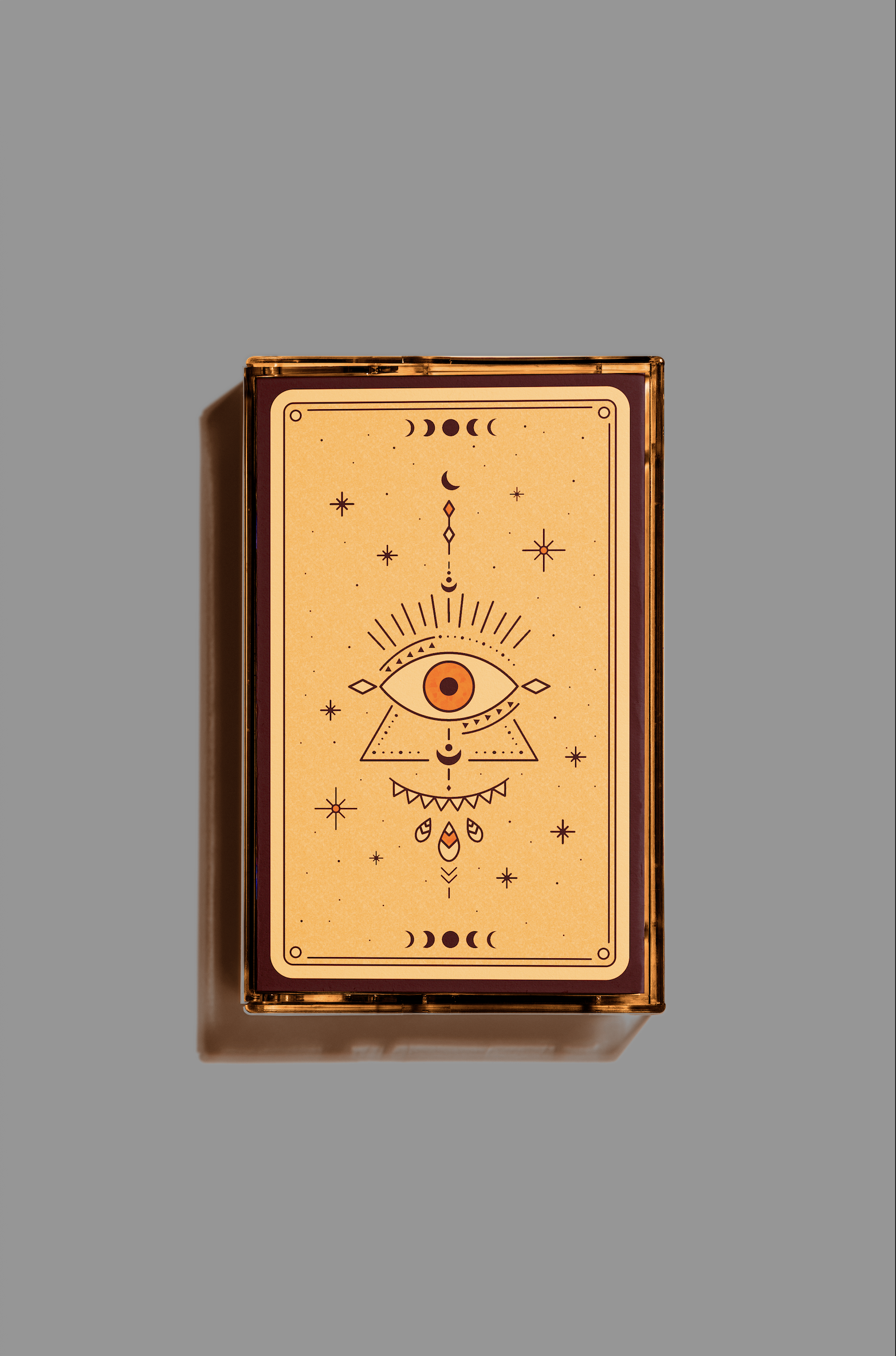 A rectangular box with tarot-like mystical symbols and celestial imagery, featuring an eye at the center, surrounded by geometric shapes, stars, moons, and decorative elements, on a light orange background.