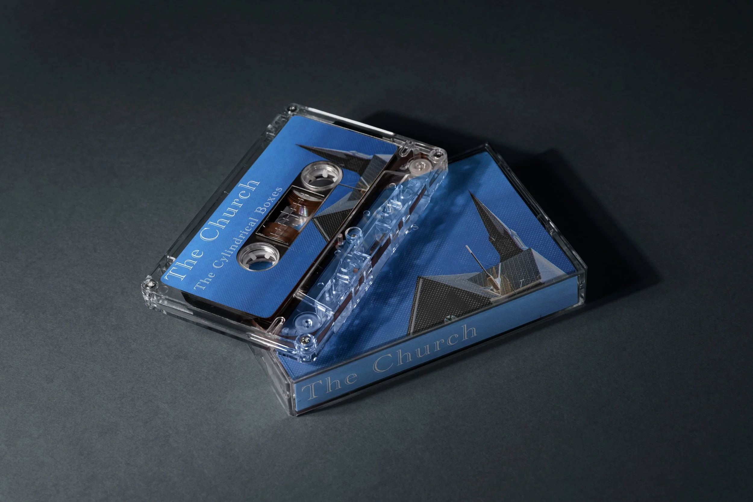 A cassette tape titled 'The Church: The Cautionary Tales' inside a transparent case with a blue cover art of a church building.