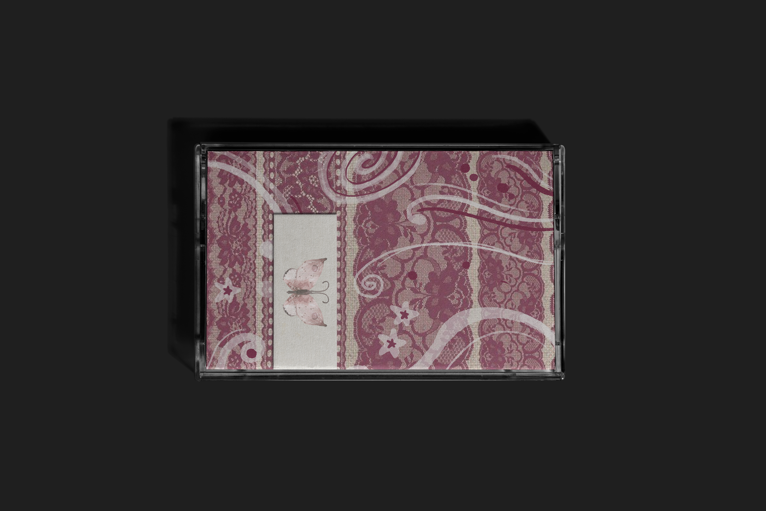 A rectangular box with a floral and butterfly pattern in pink and beige, seen from the top, with a black border on a dark background.