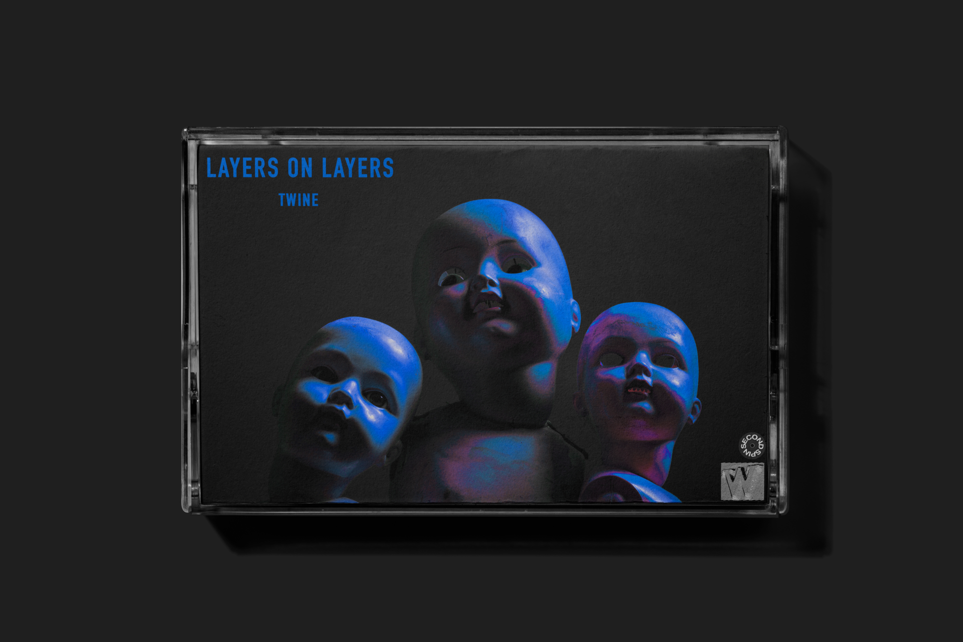 A cassette tape case featuring an album cover with three eerie, blue-tinted baby dolls against a black background. The album title 'Layers on Layers' and artist name 'Twine' are written in blue text in the top left corner.