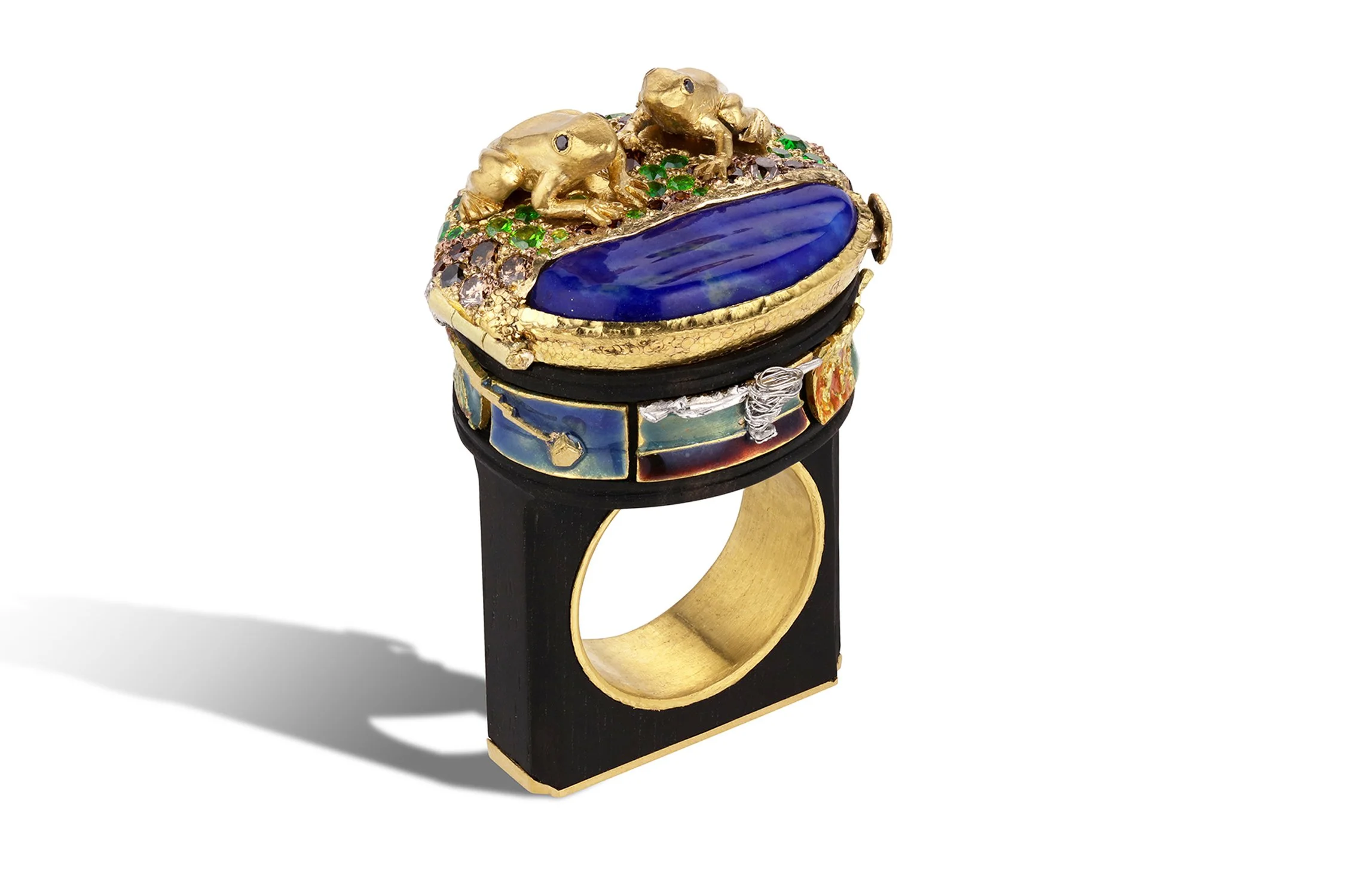 A decorative ring featuring gold frogs sitting on a textured, gold and enamel band with colorful details and a large, blue, oval-shaped stone on top.