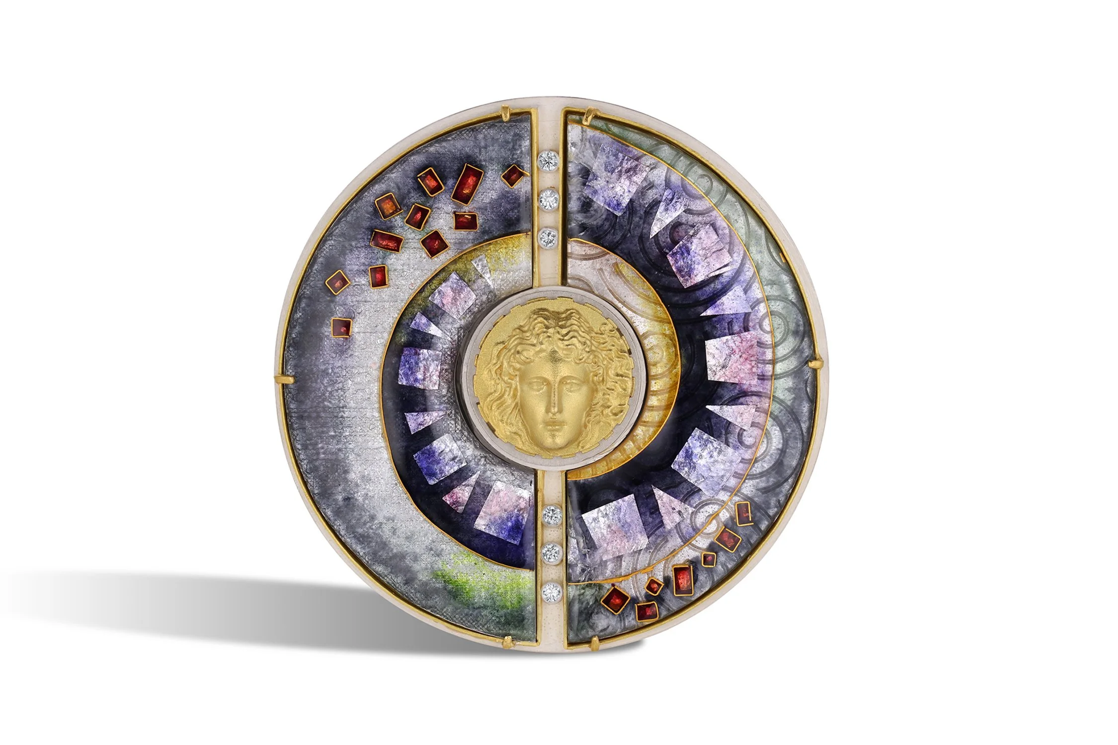 A round clock or decorative piece featuring a gold Medusa head at the center with various colored stones, gemstones, and intricate patterns surrounding it.