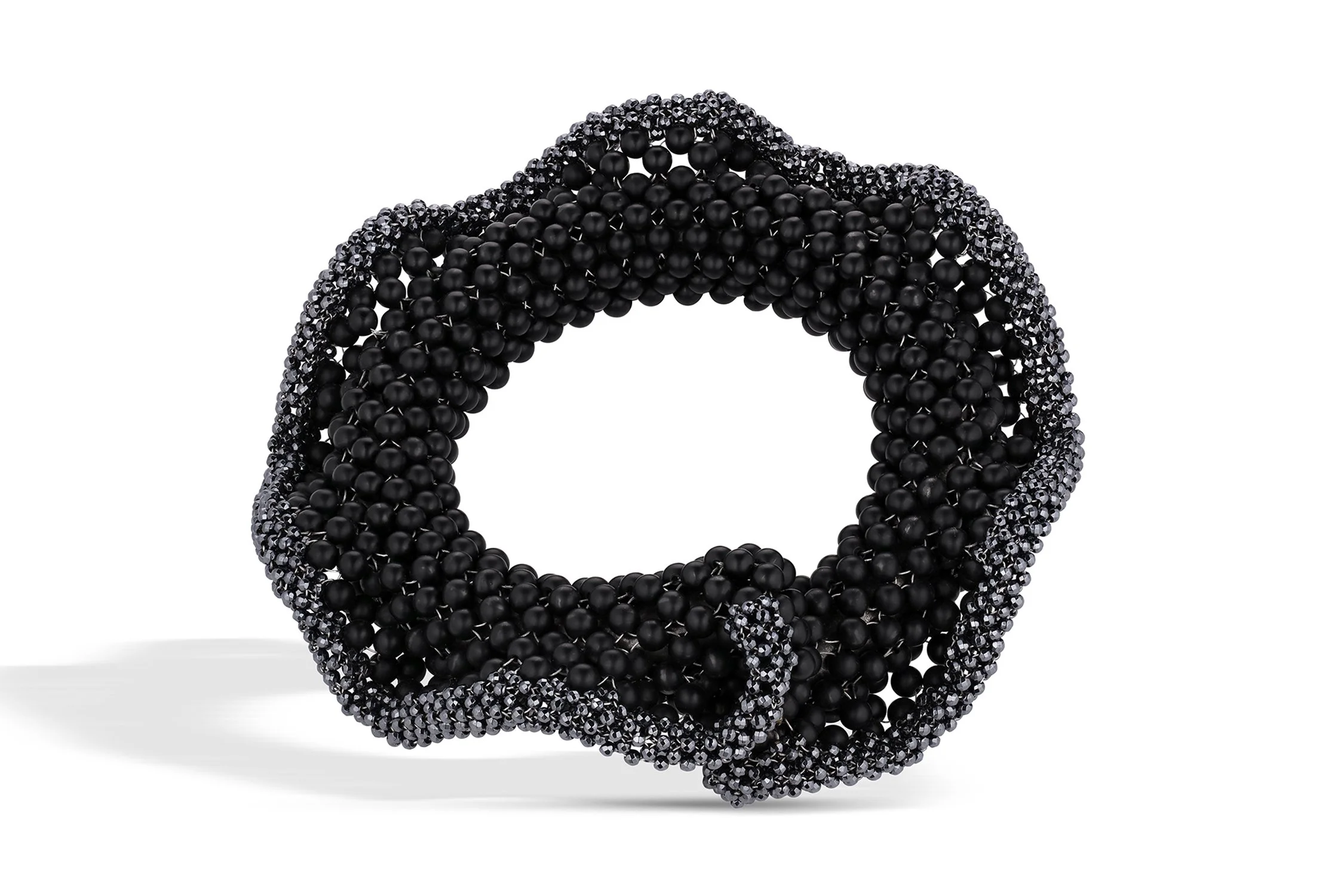 A circular fashion accessory or jewelry piece made of black beads, featuring a pattern of larger matte black beads surrounded by smaller, shiny black beads.