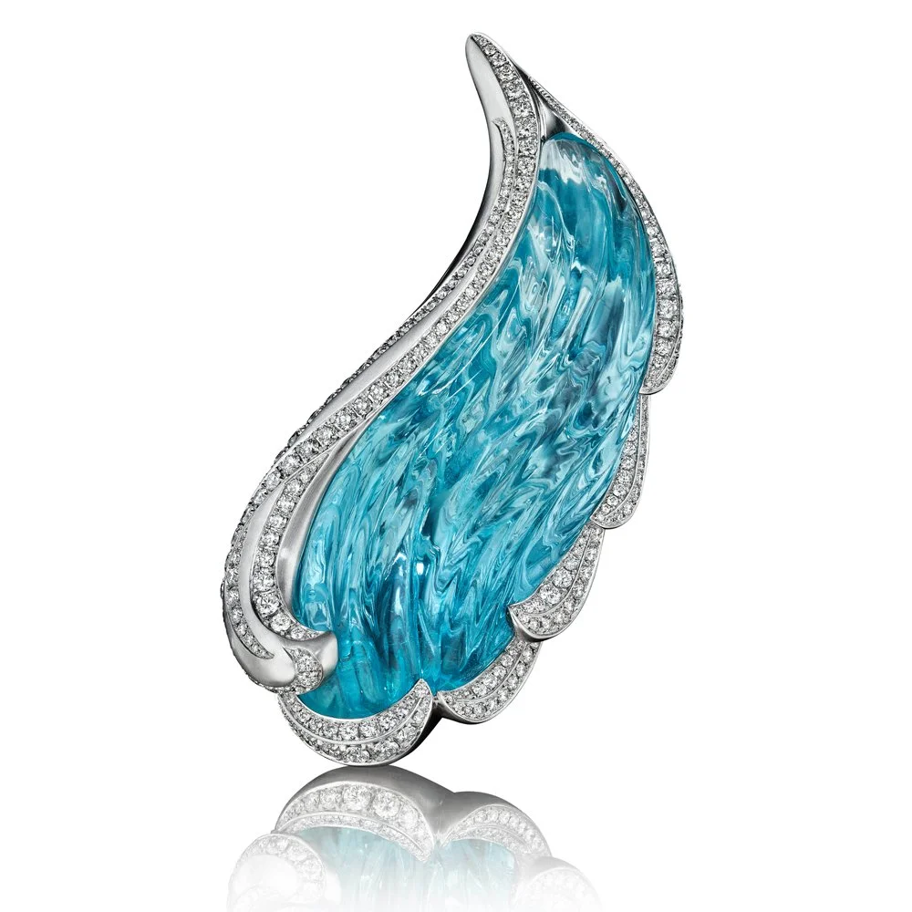 A jewelry brooch with a large, blue, feather-shaped gemstone accented by small diamonds, set in silver or white gold.