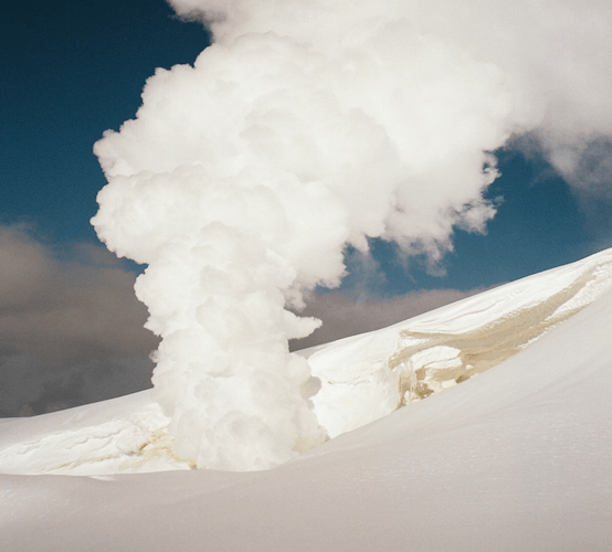 A volcano erupting in a snowy landscape with white smoke and steam rising into the sky.