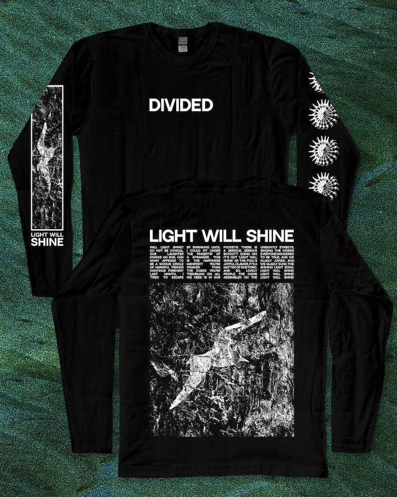Two black long-sleeve shirts with white text and graphics are displayed on a glittery green background. The top shirt has the word "DIVIDED" written across the chest. The bottom shirt features the phrase "LIGHT WILL SHINE" and a block of white text, 