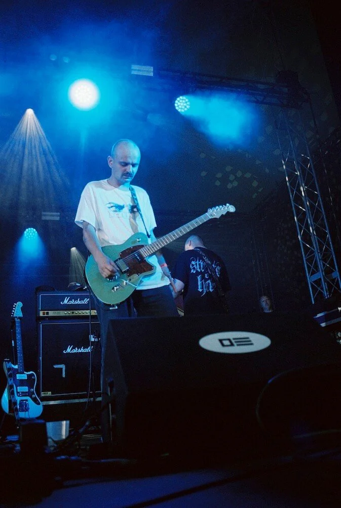 Divided Live - A musician playing an electric guitar on stage, with blue stage lights and Marshall amplifiers in the background.