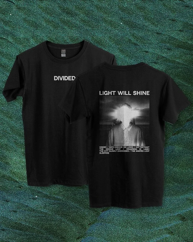 Two black T-shirts with graphic and text designs laid on a green textured background. The front shirt has the word "DIVIDED" in white for the text. The back shirt has the phrase "LIGHT WILL SHINE" along with a black-and-white image of a person with a
