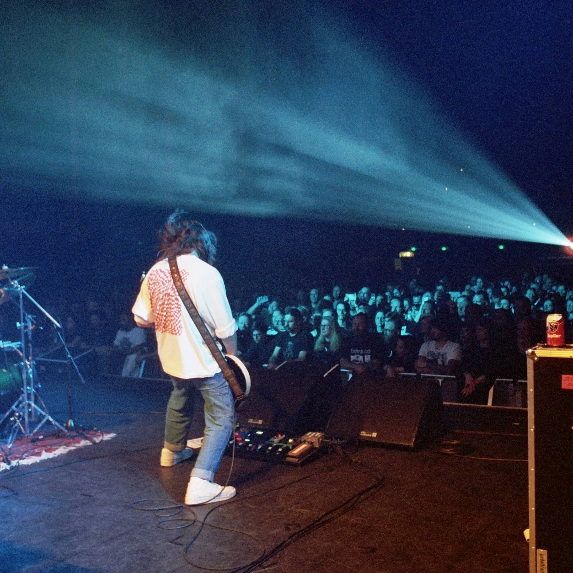 Divided Live - Musician with long hair playing guitar on stage in front of audience in a dark concert hall with blue and yellow stage lighting.