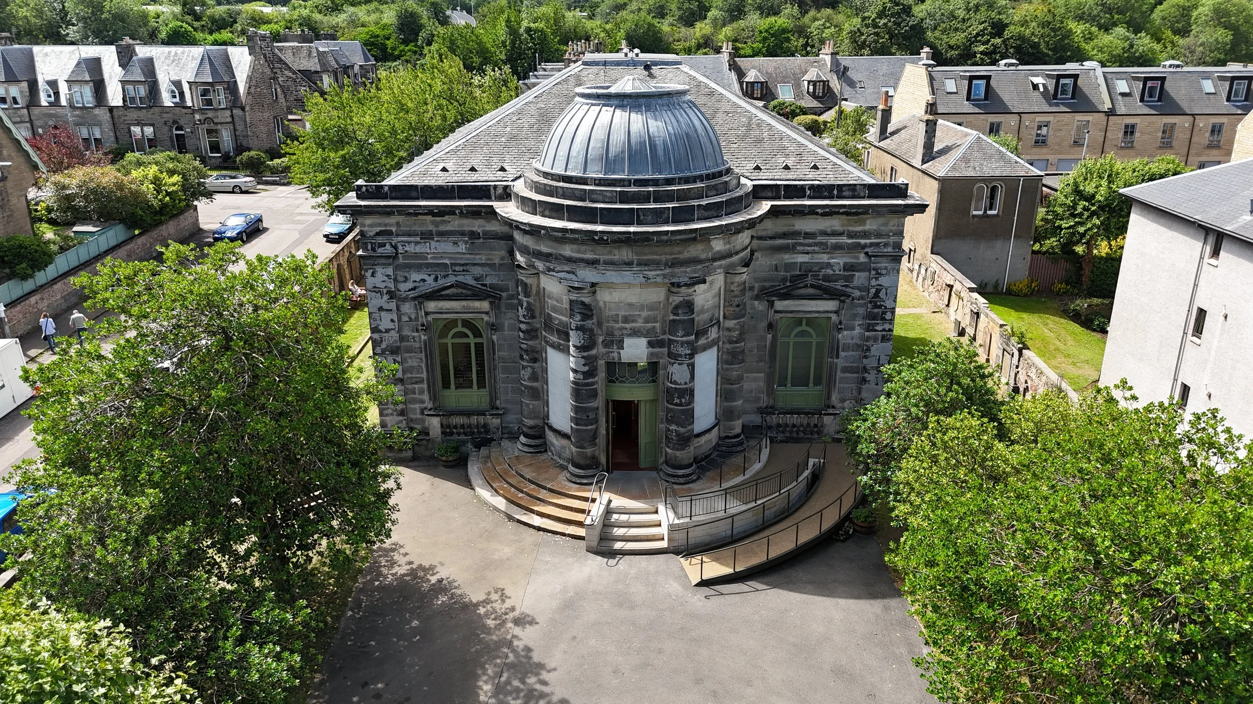 Taft Architects — An aerial view of a historic stone church with a curved entrance and round dome, surrounded by trees and residential buildings.
