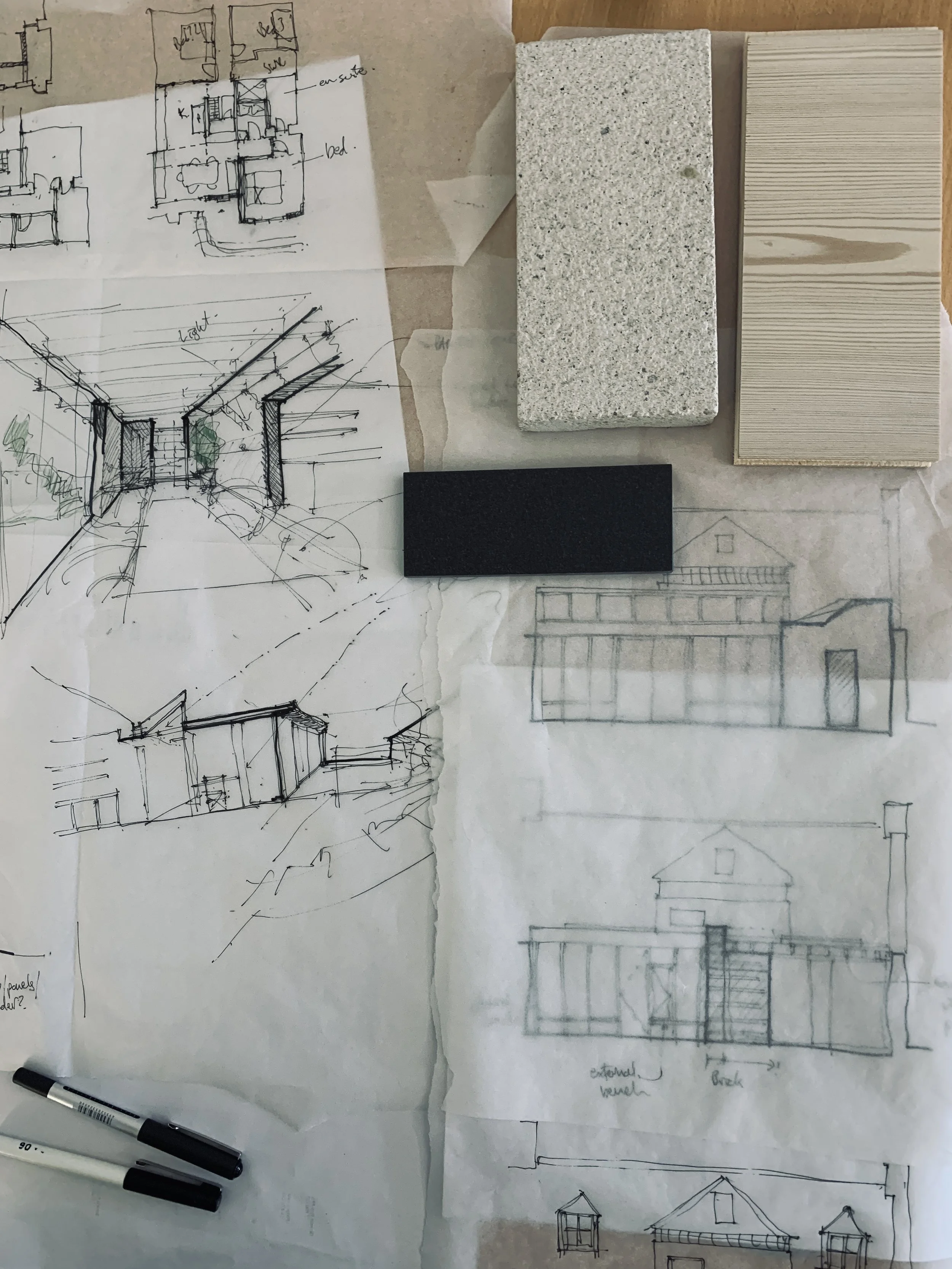 Architectural sketches and design plans for a building, with sample materials including concrete, wood, and black material, along with handwritten notes and drawings.