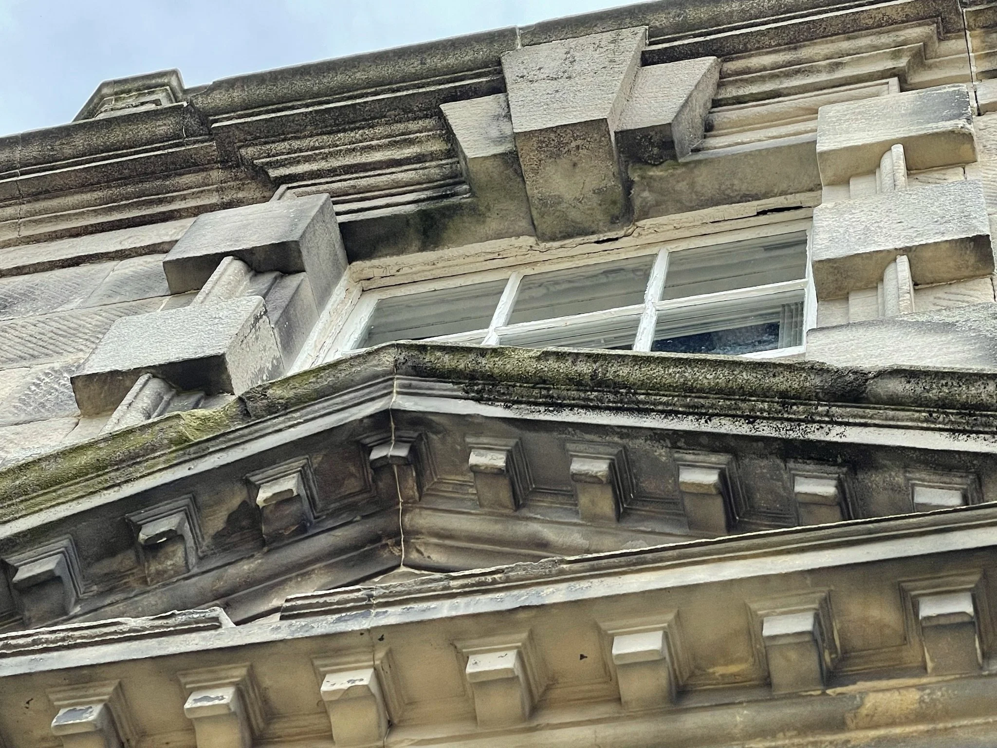 Close-up of an ornate building corner with old stonework, cornices, and a window.