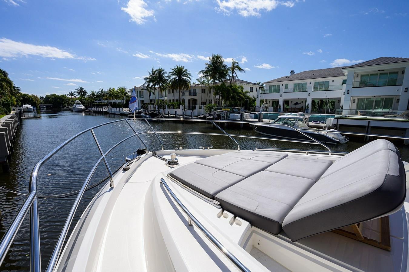 View from a yacht on a canal with modern houses, palm trees, and other boats docked along the water under a sunny sky.