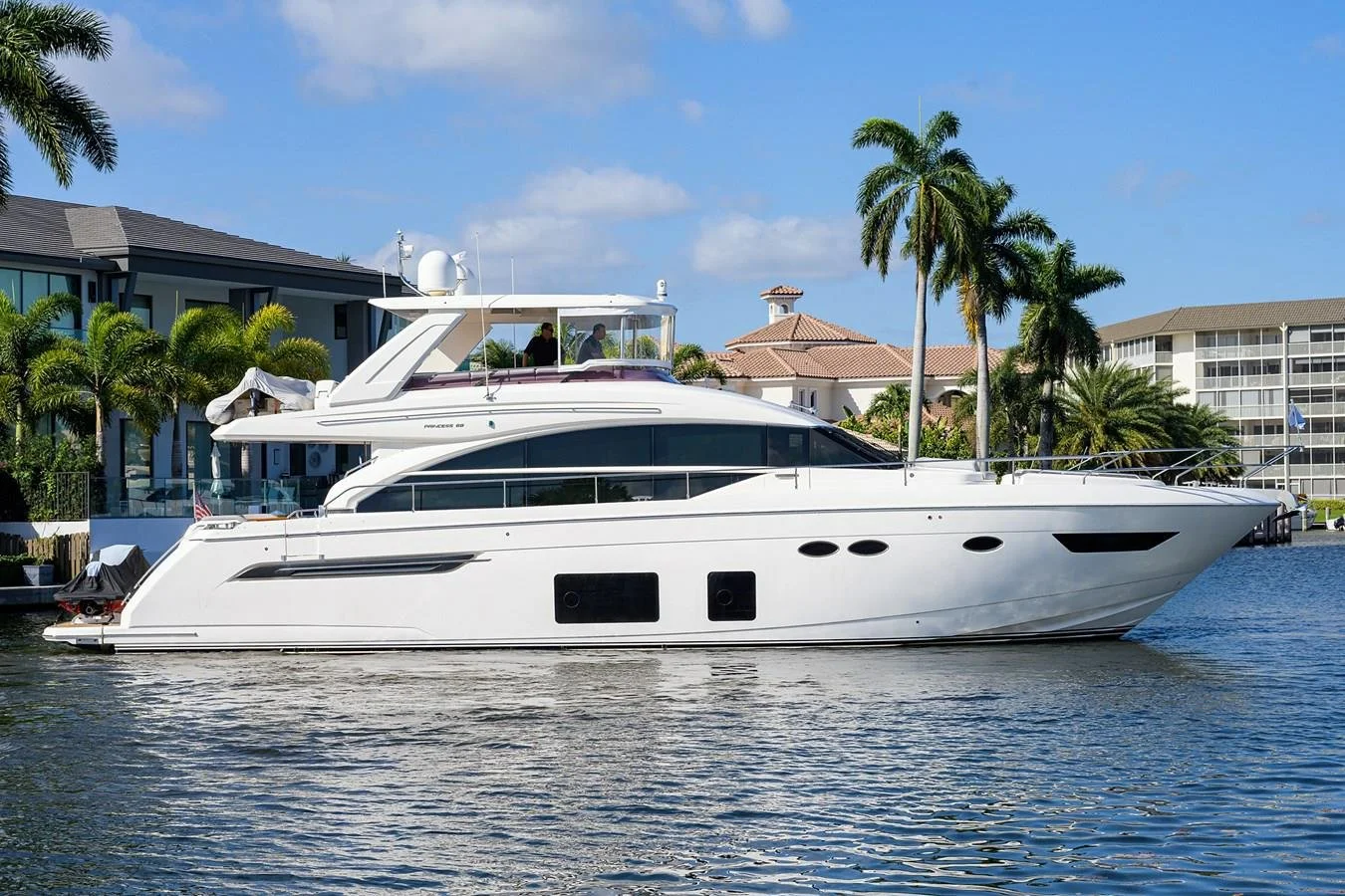 White luxury yacht with palm trees and waterfront houses in the background on a sunny day.