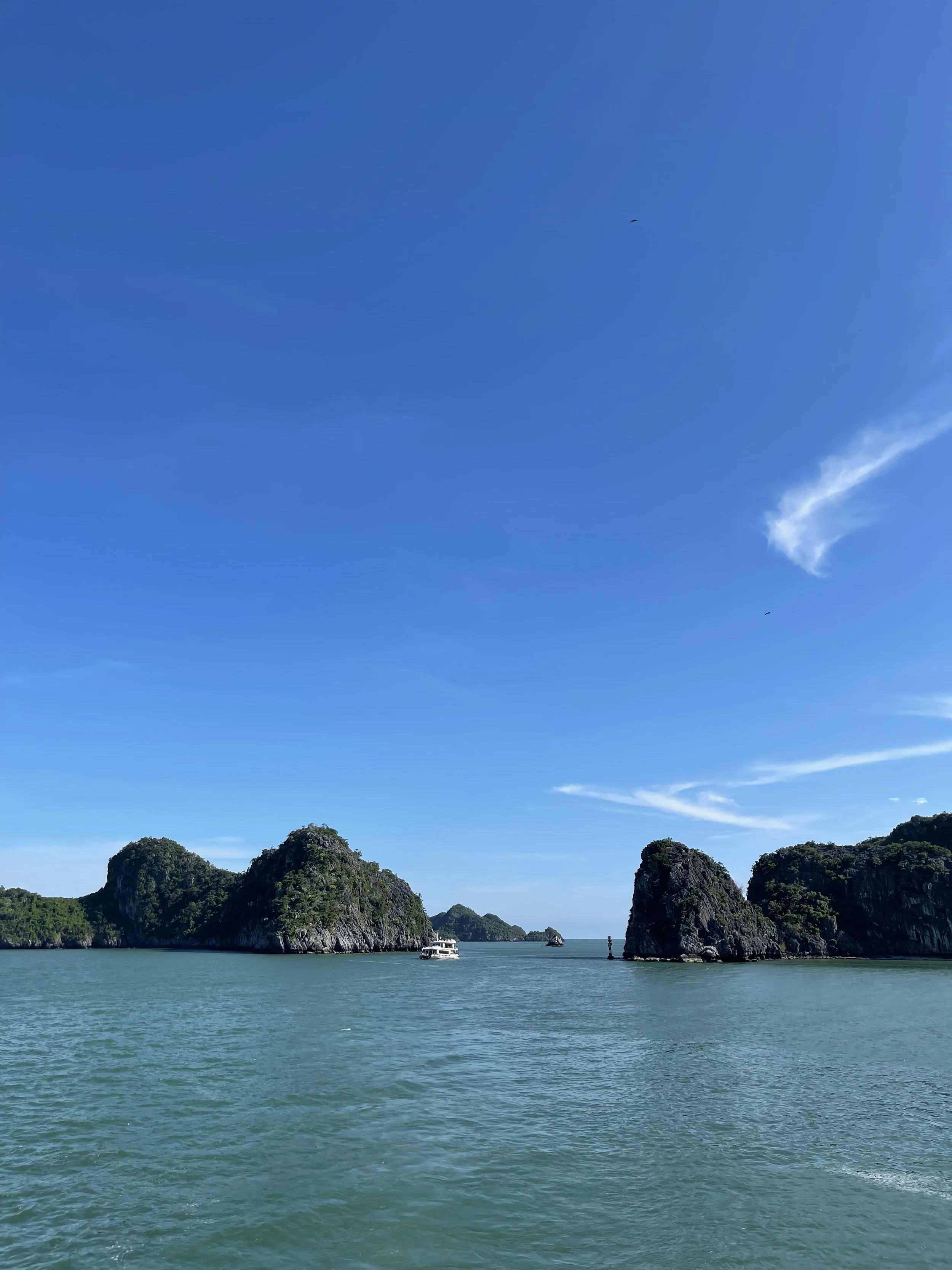 Blick auf das Meer mit mehreren Felseninseln und einem Boot unter einem klaren blauen Himmel.
