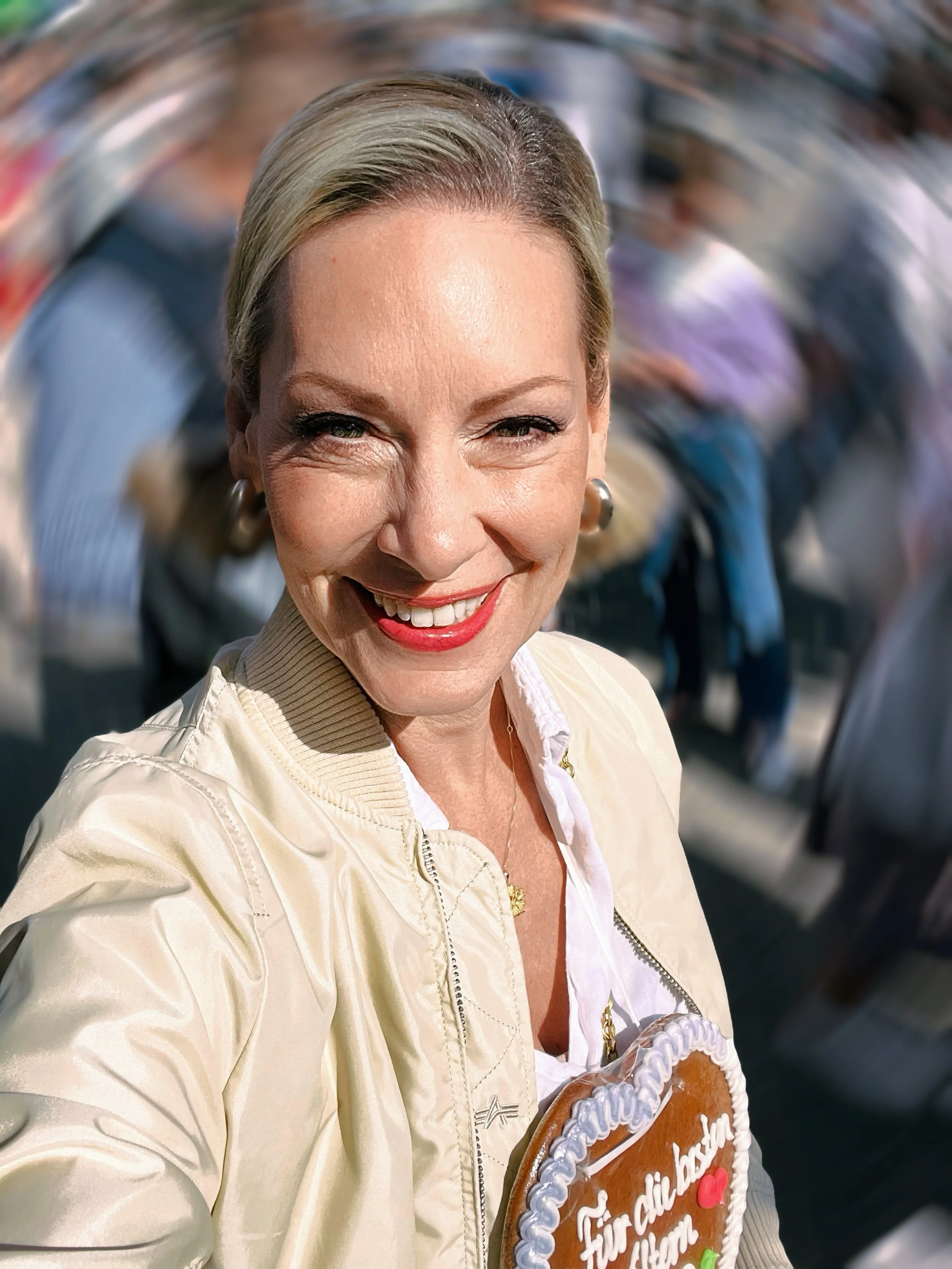 Eine lachende Frau hält ein Lebkuchenherz mit der Aufschrift 'Für dich liebe Mama'.