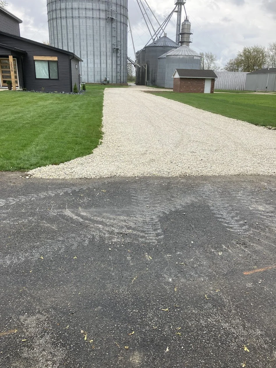 Gravel driveway leading to farm buildings, silos, and greenery.