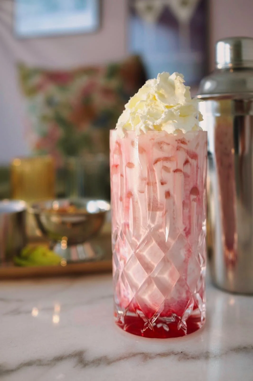 Ein Glas mit pinkfarbenem Milchshake, garniert mit geschlagener Sahne, auf einem weißen Marmortisch.