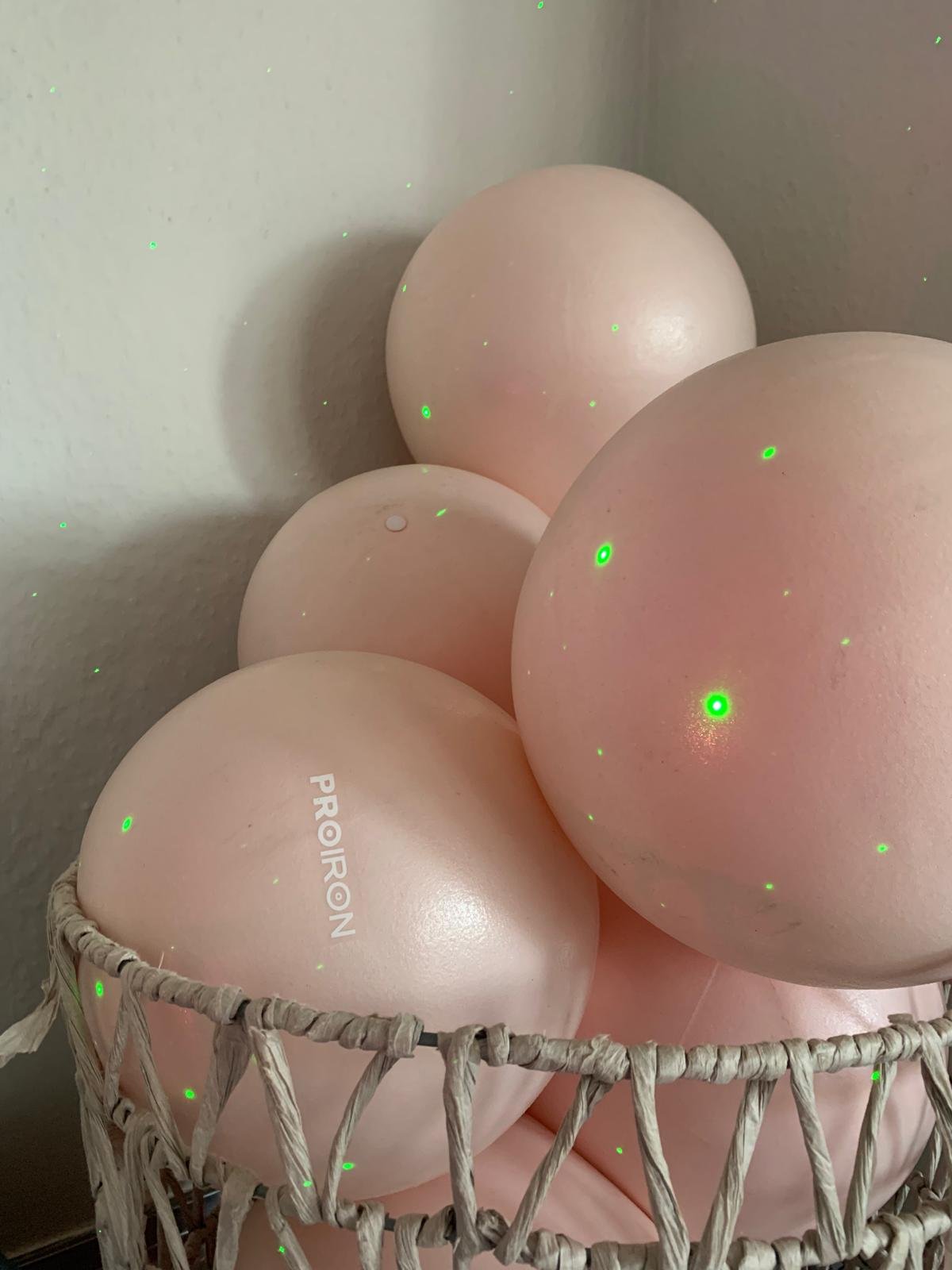 A basket containing five small exercise balls with green laser dots scattered over them, with one egg displaying the word 'PROIRON' printed on it.