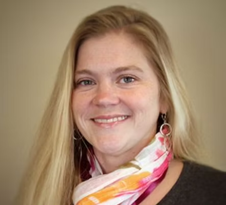 Portrait of a smiling woman with long blonde hair, wearing earrings and a colorful scarf.