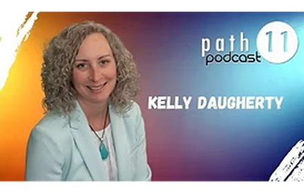 A woman with curly gray hair wearing a light blue blazer and turquoise necklace, smiling in front of a colorful background with the text 'path 11 podcast' and 'Kelly Daugherty'.