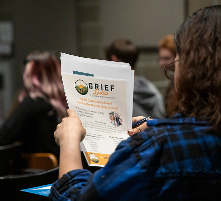Person holding a flyer at a community event, with other attendees in the background.