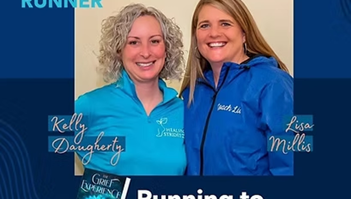 Two women standing side by side smiling at the camera, wearing blue jackets with professional logos, indoors with a plain background.