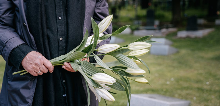 Person holding a bouquet of white lilies outdoors near a cemetery.