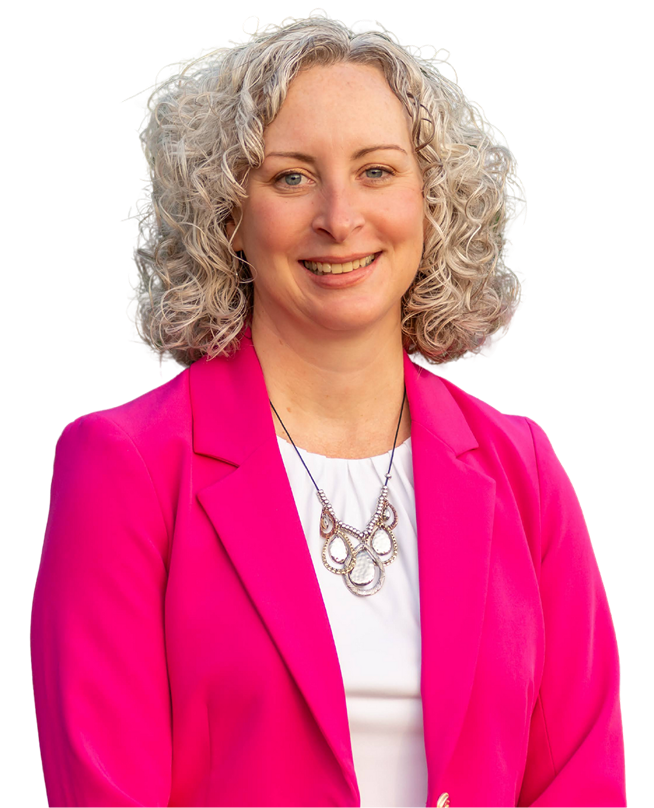 A woman with curly blonde hair smiling, wearing a pink blazer, white top, and a silver necklace.