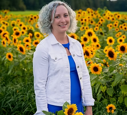 A woman with curly gray hair smiling in a sunflower field