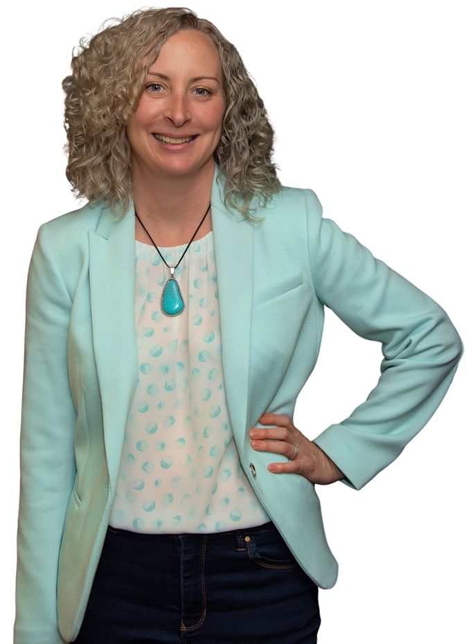 A woman smiling, wearing a light blue blazer, white blouse with light blue polka dots, and a turquoise necklace, standing with her hand on her hip.