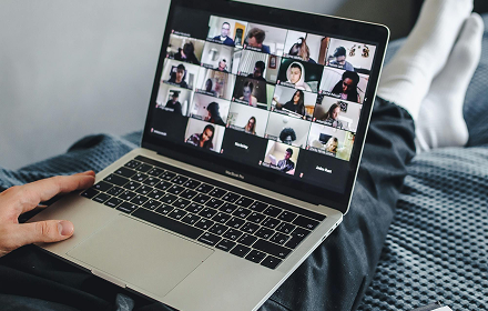 Person using a laptop for a virtual meeting with multiple participants displayed on the screen