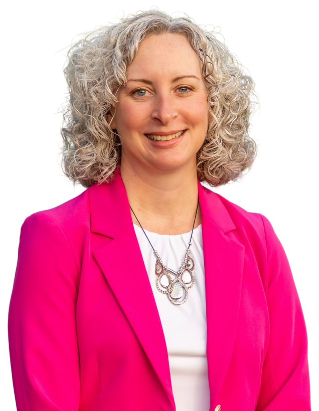 A smiling woman with curly gray hair wearing a bright pink blazer over a white top and a silver necklace.