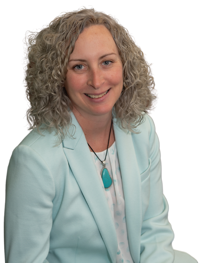 A woman with curly blonde hair smiling, wearing a light blue blazer and a turquoise pendant necklace.